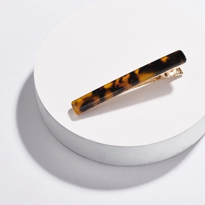 Minimalist tortoiseshell acrylic hair clip with golden metal base on a white podium