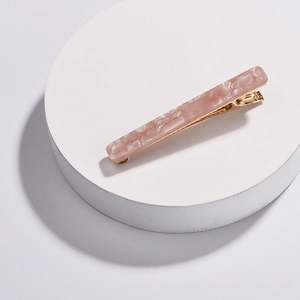 Detailed view of pink marble acetate hair clip with golden metal base on white stand