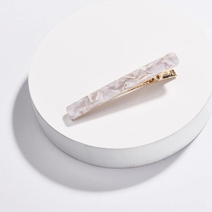 Close-up of white marble pattern hair clip with gold metal base on a white platform
