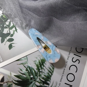 Close-up of light blue marble acrylic hair clip with gold metal spring on mesh fabric