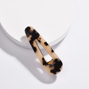 Detail of tortoise shell acrylic hair clip with golden metal duckbill clamp on white stand