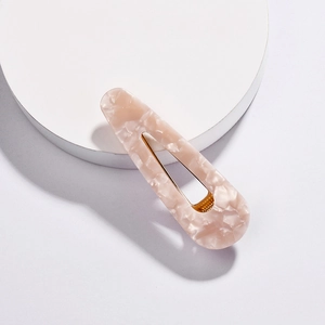 Detail of pink marble acetate hair clip with golden metal base on a white stand