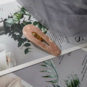 Detailed view of a pink marble resin hair clip with a gold metallic base on a magazine