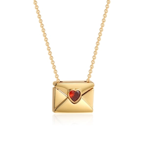 Macro shot of an 18K gold envelope pendant featuring a red heart zircon and a fine O-chain