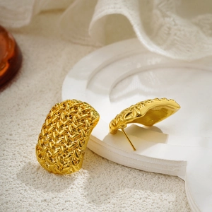 Detalle macro de pendientes geométricos trenzados en oro de 18K sobre una bandeja