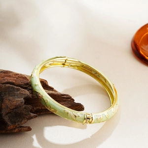 Detailed view of light green enamel bangle with golden floral carvings and hinge clasp
