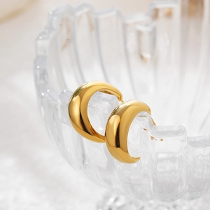 Nahaufnahme klobiger goldener C-Ohrringe, hängend an einer strukturierten Glasschale