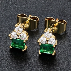 Macro shot of 18K gold plated earrings with emerald green square stones on black background