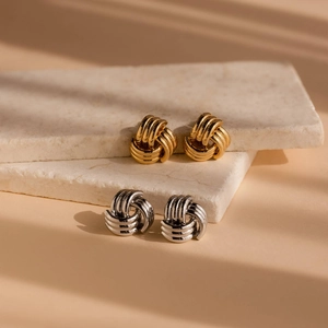 Dettaglio di orecchini a nodo oro e argento su marmo bianco con ombre eleganti