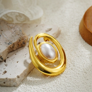 Elegant 18k gold spiral brooch with a central pearl set on a textured stone surface