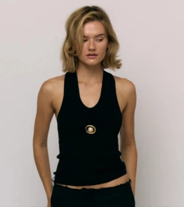 Detail of a 18k gold spiral brooch with pearl on a black ribbed knit sleeveless top