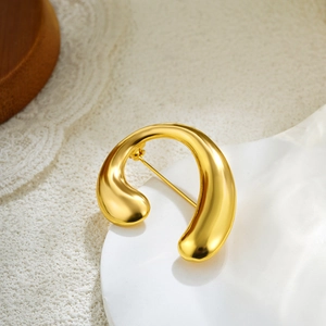 Detailed macro view of 18k gold pearl brooch with polished abstract curved surface
