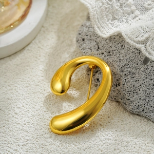Polished 18k gold spiral pearl brooch with abstract curves on white marble background
