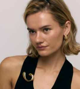 Close-up of polished 18k gold spiral brooch and striped earrings on a black outfit