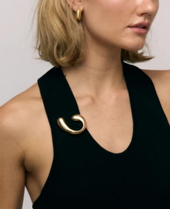 Detail of 18k gold spiral brooch and textured hoop earrings on black knitwear