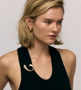 Close-up of minimalist 18k gold spiral brooch and cylindrical earrings on a model