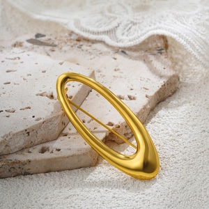 Macro detail of 18k gold polished pearl spiral brooch on textured travertine stone