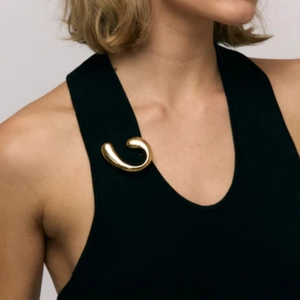 Elegant 18k gold fluid spiral brooch with glossy pearl on a black vest top