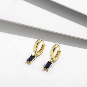 Detalle de pendiente bañado en oro 14K con circón azul rectangular sobre fondo blanco