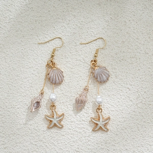 Détail des boucles d'oreilles étoile de mer perles or 14K avec coquillages et pompons