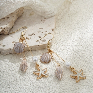 Détail de boucles d'oreilles en or 14K avec perles, coquillages et breloques d'étoile de mer