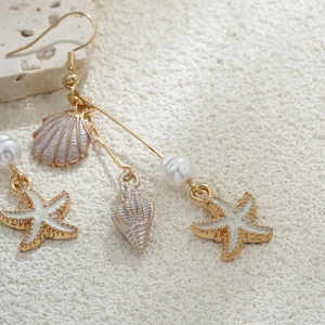 Vue macro de boucles d'oreilles étoile de mer en or 14K avec perles sur sable blanc