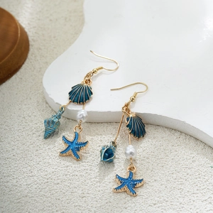 Détail de boucles d'oreilles coquillage en or 14K avec perles sur décor sable
