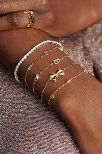 Detailed view of layered 18K gold-plated bracelets and Mrs ring on a model's wrist