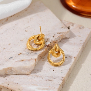 Detalle de pendientes de aro dobles entrelazados de oro de 18K sobre base de mármol