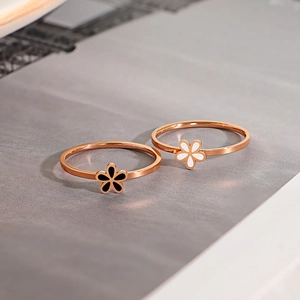 Minimalist rose gold daisy rings with black and white flower charms on a grey background