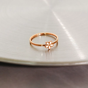 Detailed view of rose gold daisy ring with white enamel flower on metal background