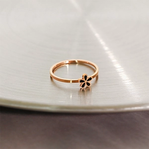 Close-up of rose gold daisy ring with black enamel flower on a brushed metal tray