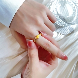 Nahaufnahme des goldenen Herz-Kettenrings am Finger vor elegantem weißem Hintergrund