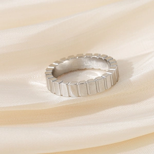 Close-up of a silver ring with vertical grooves on a cream silk background