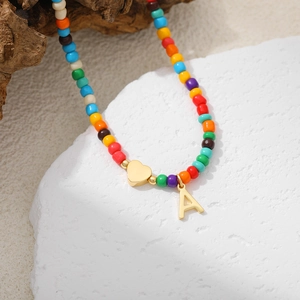 Detail of colorful beaded necklace with golden heart and letter A pendant on white stone