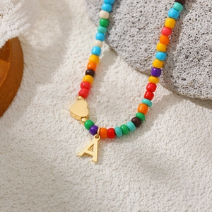 Close-up of a rainbow beaded necklace with gold heart and letter A pendant on a stone