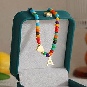 Macro view of 14k gold heart and A-letter charms on a colorful beaded rainbow necklace