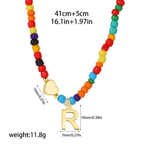 Detail of colorful beaded necklace featuring a 14k gold heart and letter R pendant charm