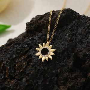 Detail of 18K gold plated sunflower pendant with pavé zircons on black volcanic rock