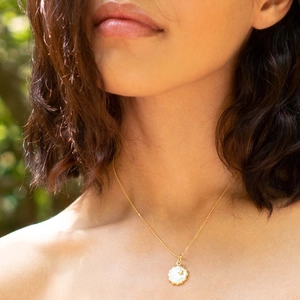 Close-up of 18K gold-plated compass pendant with white shell and star on a model