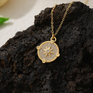 Macro shot of 18K gold plated compass pendant with zircon star on black volcanic stone