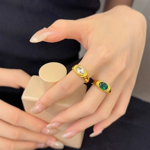 Close-up of vintage 18K gold ring set with green emerald and oval zircon on finger