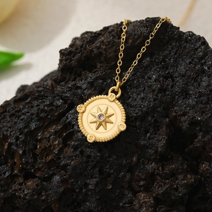 Detail of 18K gold plated compass pendant with starburst and zircon on volcanic stone