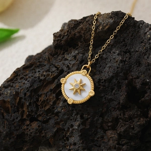 Detail of 18K gold compass necklace with zircon star and mother of pearl on dark rock