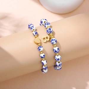 Detail of beaded bracelet featuring blue floral ceramic beads and gold heart pendant