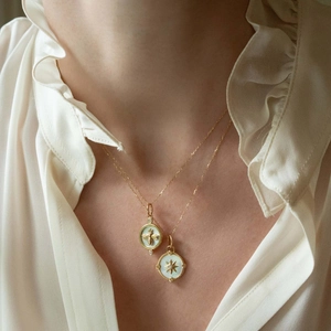 Detailed macro view of 18K gold plated compass and bee pendants with white shell inlay