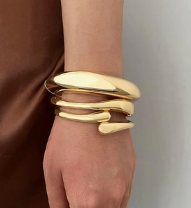 Close-up of a three-piece gold liquid metal bangle set with high-polish finish