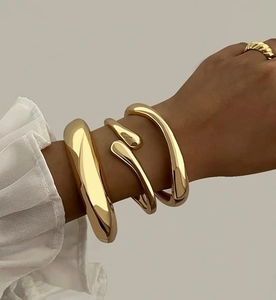 Detailed view of three polished 14K gold-plated bracelets and a matching twist ring