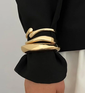 Close-up of three 14K gold plated stacked bracelets on a black long sleeve background