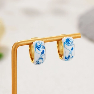 Detail of 18K gold C-shaped hoop earring with blue marble enamel on a jewelry stand